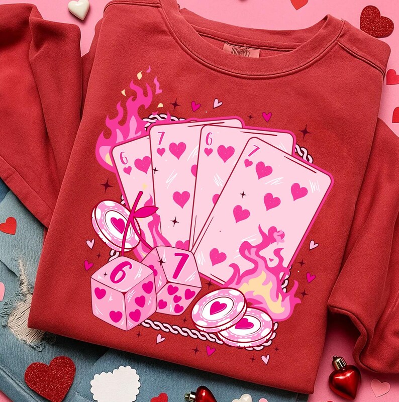 May include: Red sweatshirt featuring a graphic of playing cards, dice, and poker chips with heart symbols. The design includes pink flames and a rope border. The sweatshirt is a solid red color.