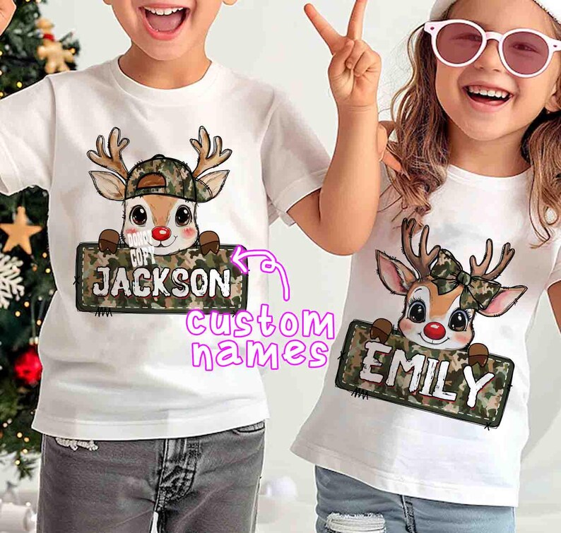 May include: Two white t-shirts with a cartoon reindeer design. The reindeer wears a camouflage hat and holds a sign with a custom name. One shirt says "JACKSON" and the other says "EMILY".