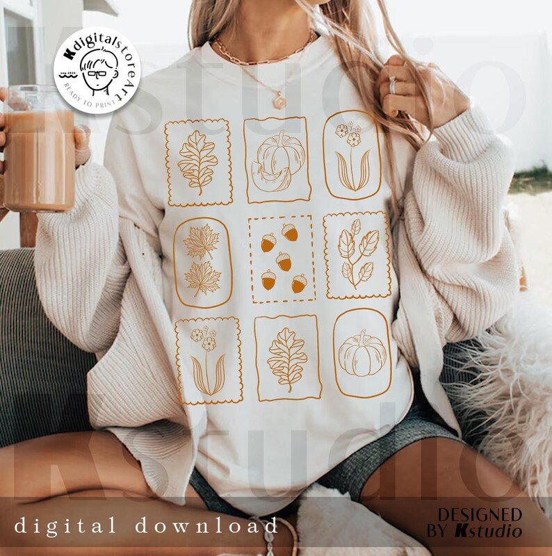 May include: White sweatshirt featuring a grid of autumn-themed illustrations in orange, including leaves, pumpkins, and acorns. The words "digital download" are printed at the bottom. The design is by Kstudio.