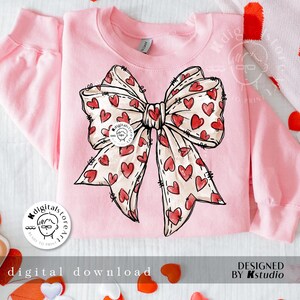 May include: Pink sweatshirt with a large, hand-drawn bow with hearts on it. The bow is in shades of pink and red.