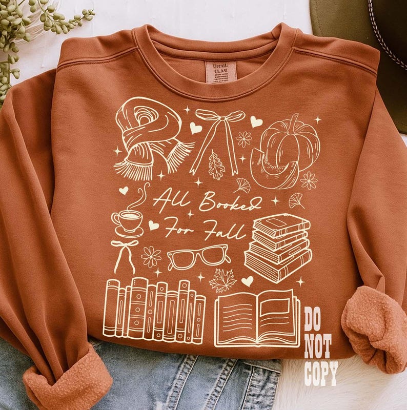 May include: Rust-colored sweatshirt with a white graphic design featuring a scarf, bow, pumpkin, books, coffee cup, glasses, and the text "All Booked For Fall." The design also includes the text "DO NOT COPY."