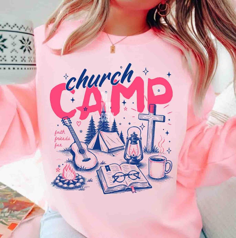 K&ouml;nnte beinhalten: Rosa Sweatshirt mit einem grafischen Design mit den Worten "church CAMP" in Blau und Pink. Das Design umfasst eine Gitarre, ein Zelt, ein Lagerfeuer, ein Kreuz, eine Laterne, ein offenes Buch und eine Kaffeetasse. Die Worte "faith friends fun" sind ebenfalls enthalten.