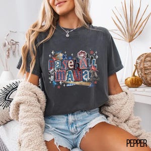 K&ouml;nnte beinhalten: Dunkelgraues T-Shirt mit dem Text "Baseball Mama" in einer Collage aus rot-wei&szlig;-blauen Baseball-Grafiken. Das Shirt hat einen bequemen, l&auml;ssigen Stil.