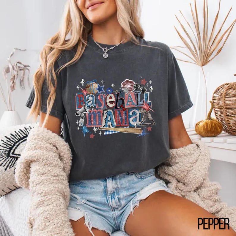 K&ouml;nnte beinhalten: Dunkelgraues T-Shirt mit dem Text "Baseball Mama" in einer Collage aus rot-wei&szlig;-blauen Baseball-Grafiken. Das Shirt hat einen bequemen, l&auml;ssigen Stil.