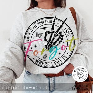 May include: A gray sweatshirt with a black and white graphic print of a skeleton hand making a peace sign. The graphic is surrounded by a circle with the text "I have it all together I just forgot where I put it". The text is in a rainbow of colors.