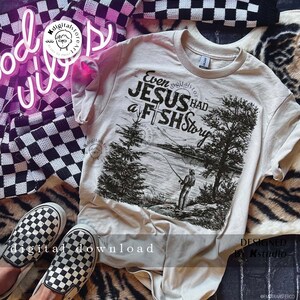 May include: A beige t-shirt with a black and white graphic print of a person fishing. The graphic includes the text "Even Jesus Had a Fish Story".