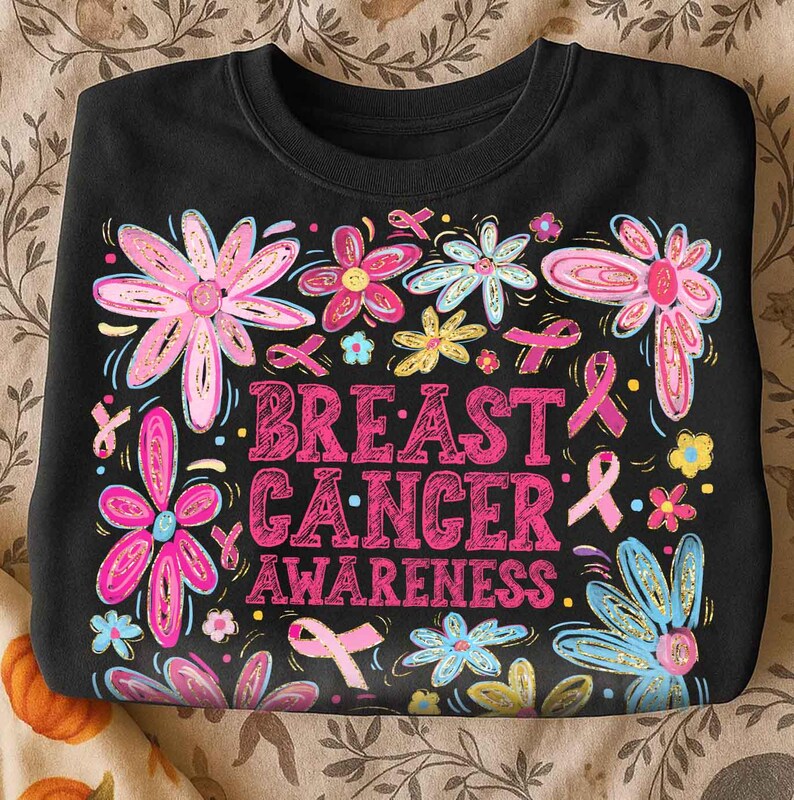 May include: Black crewneck sweatshirt with a floral design and the words "Breast Cancer Awareness" in pink. The flowers are pink, blue, and yellow with gold accents, and pink ribbons are scattered throughout.