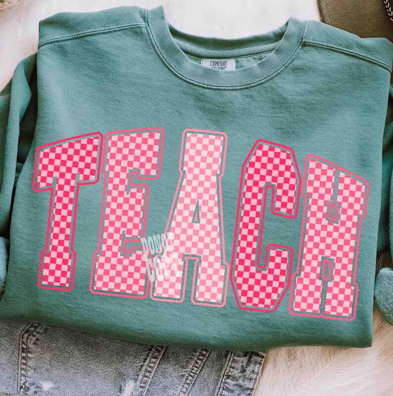 K&ouml;nnte beinhalten: Ein teal-farbenes Sweatshirt mit dem Wort "TEACH" in gro&szlig;en, rosa karierten Buchstaben. Das Sweatshirt hat einen Rundhalsausschnitt und lange &Auml;rmel. Der Text "DON'T COMPROMISE" ist unter dem Buchstaben "A" aufgedruckt.
