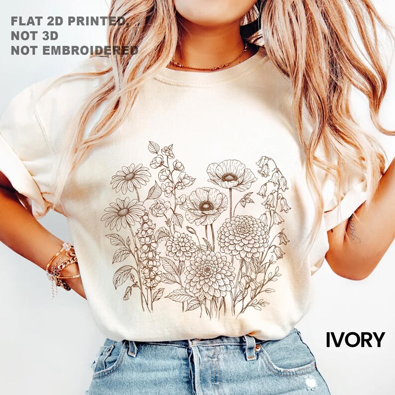 May include: Ivory-colored t-shirt featuring a detailed floral line drawing. The design includes daisies, poppies, and other flowers. The text "FLAT 2D PRINTED, NOT 3D, NOT EMBROIDERED" is printed at the top, and "IVORY" is printed at the bottom.