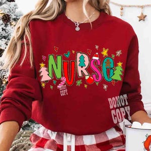 May include: A red sweatshirt with the word "NURSE" in colorful, festive lettering. The letters are decorated with Christmas-themed images like trees, ornaments, and gingerbread men. The text "DONOT COPY" is printed on the bottom.