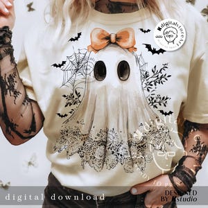 May include: Cream-colored t-shirt featuring a ghost illustration with a bow, lace details, and bat silhouettes. The ghost has large black eyes and a lace-trimmed bottom. The text "digital download" is at the bottom.