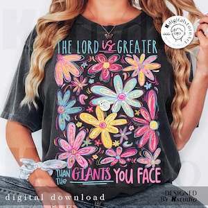 May include: Dark gray t-shirt with a colorful floral design and the text "THE LORD IS GREATER THAN THE GIANTS YOU FACE." The flowers are in shades of pink, yellow, blue, and green. The words "digital download" are at the bottom.