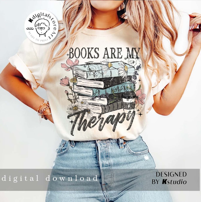 K&ouml;nnte beinhalten: Ein wei&szlig;es T-Shirt mit dem Aufdruck "BOOKS ARE MY THERAPY". Der Text ist von einem Stapel B&uuml;cher und Blumen umgeben.