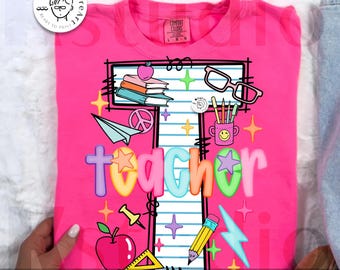 以下が含まれることがあります： 鮮やかなピンク色のTシャツ。教師向けのカラフルなグラフィックデザインが特徴です。「Teacher」の文字がバブルレターで描かれ、本、鉛筆、リンゴなどの学校をテーマにしたイラストが添えられています。Comfort Colorsブランドのシャツです。