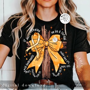 May include: A black t-shirt featuring a yellow ribbon tied in a bow on a brown cross. The text "If you're hanging on by a thread make sure it's the hem of His garment" is printed on the shirt. The text "Leukemia Awareness" is printed on the left side of the shirt. The text "Matthew 6:20-22" is printed on the bottom left side of the shirt.