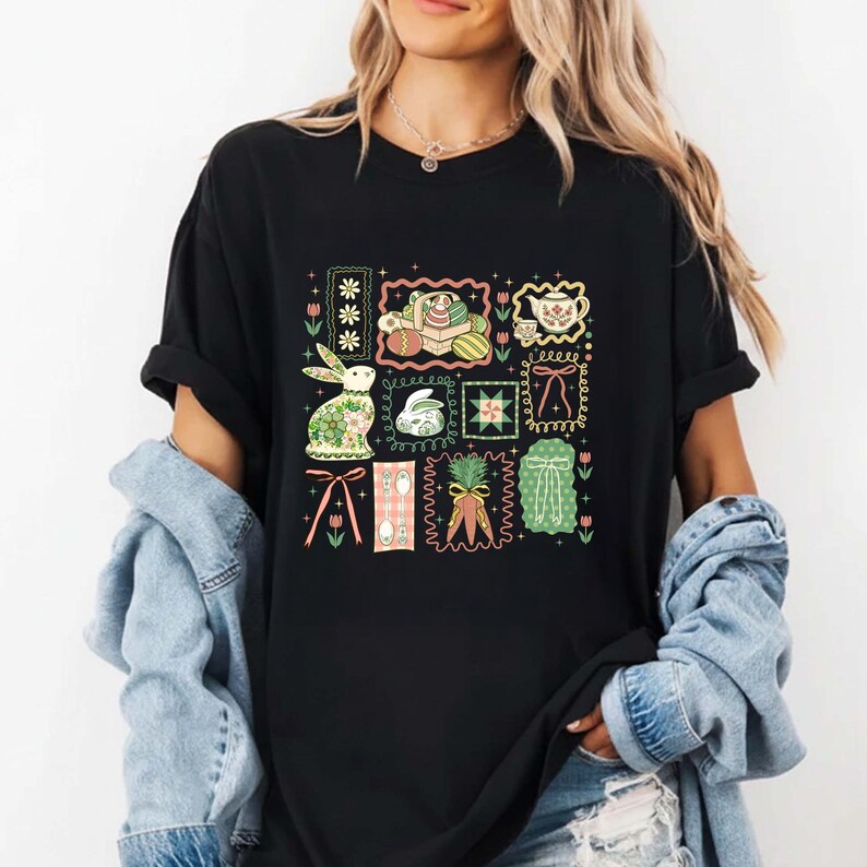 May include: Black t-shirt featuring a colorful Easter-themed graphic. The design includes a bunny, eggs, flowers, and other spring elements within decorative frames. The shirt has short sleeves and a crew neck.