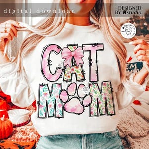 May include: White sweatshirt with a pink and floral design that says "Cat Mom" with a pink bow on the "C".