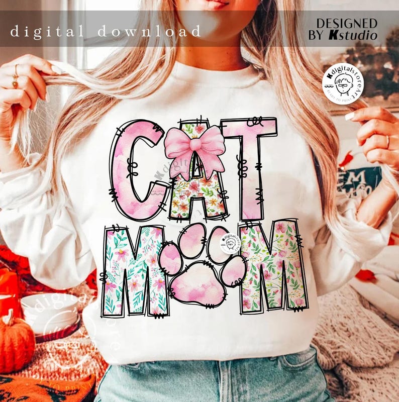 May include: White sweatshirt with a pink and floral design that says "Cat Mom" with a pink bow on the "C".