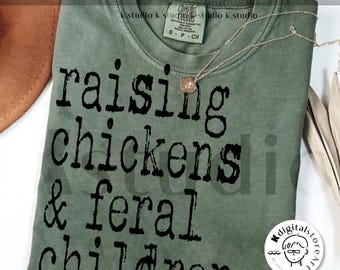 Puede incluir: Una camiseta verde con el texto "raising chickens & feral children." impreso en negro.