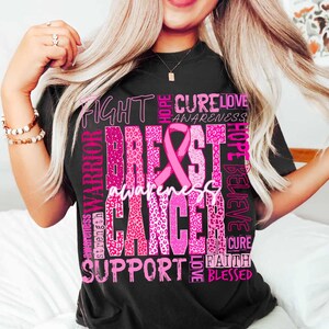 Op de afbeelding: Zwart T-shirt met een roze ontwerp voor borstkankerbewustzijn. Het ontwerp bevat een roze lint, de woorden "Breast Cancer Awareness" en andere woorden zoals "Fight", "Cure", "Hope" en "Support".