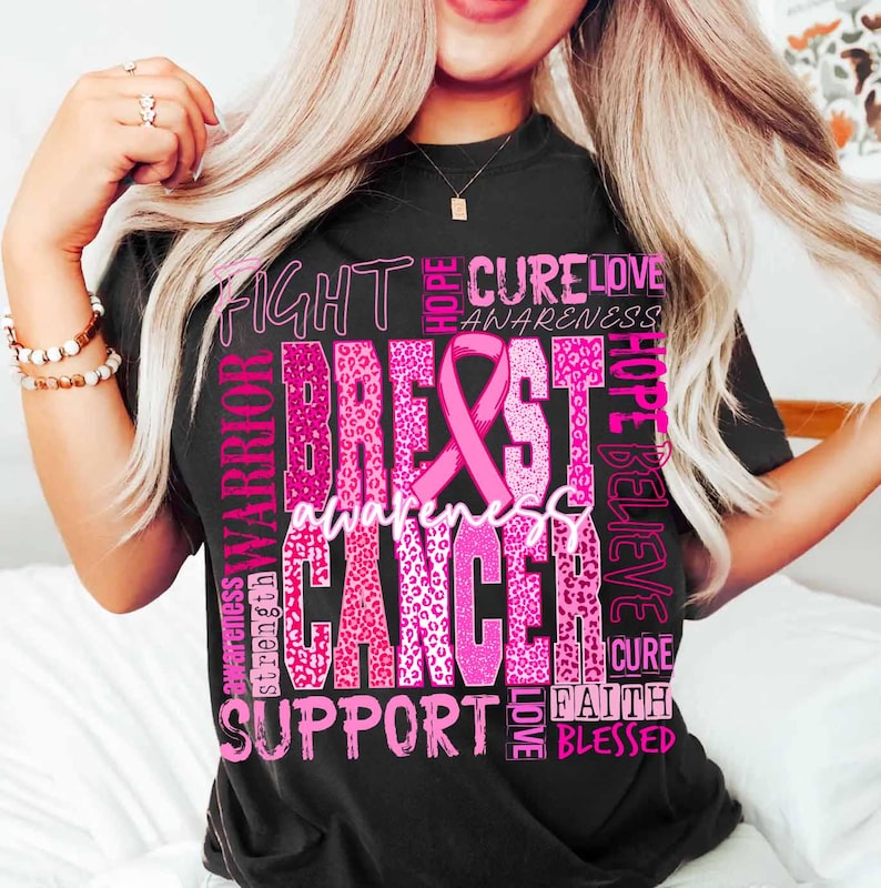 Op de afbeelding: Zwart T-shirt met een roze ontwerp voor borstkankerbewustzijn. Het ontwerp bevat een roze lint, de woorden "Breast Cancer Awareness" en andere woorden zoals "Fight", "Cure", "Hope" en "Support".
