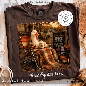 May include: A dark brown t-shirt featuring a graphic of a white goose sitting in a folding chair, wrapped in a plaid blanket, holding a mug with a pumpkin design. The text reads Pumpkin Spice & Everything Nice and Mentally I'm here.