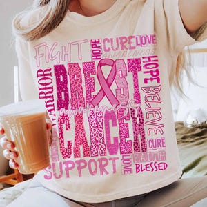 Op de afbeelding: Cr&egrave;mekleurig T-shirt met een roze borstkankerbewustzijnsontwerp. Het ontwerp bevat een roze lint, de woorden "Breast Cancer Awareness" en andere ondersteunende woorden in verschillende roze lettertypen. Het shirt is een casual stijl.