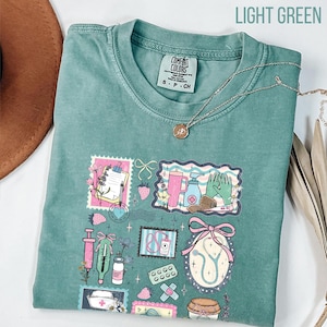Op de afbeelding: Lichtgroen T-shirt met een kleurrijk medisch thema. De afbeelding bevat illustraties van medische instrumenten, zoals een stethoscoop, spuit en verband. De tekst "LIGHT GREEN" staat bovenaan.