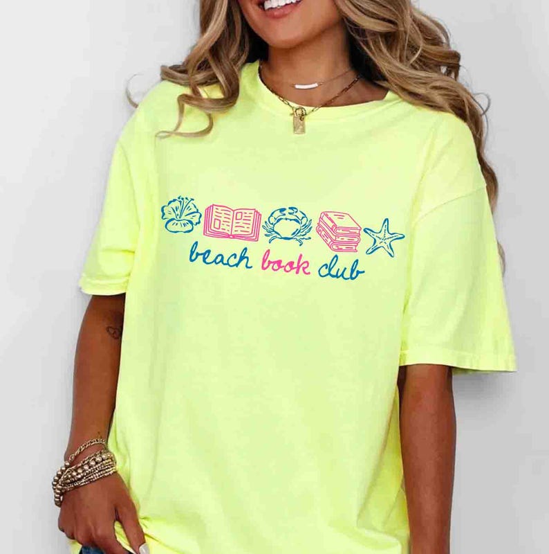 May include: A neon yellow t-shirt with a graphic that reads "beach book club" in blue script. The graphic includes illustrations of a flower, an open book, a crab, a stack of books, and a starfish, all in blue and pink.