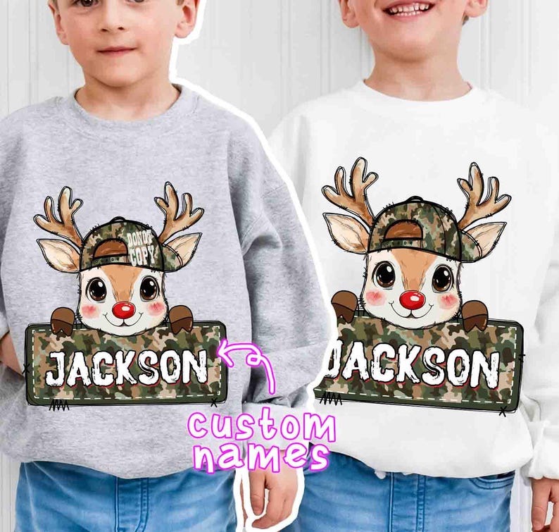 May include: Two sweatshirts, one gray and one white, each featuring a cartoon deer wearing a camouflage hat and holding a sign that says "JACKSON". The deer has a red nose and brown antlers. The sweatshirts are custom name designs.
