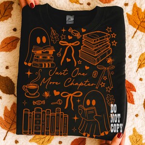 May include: Black sweatshirt with orange illustrations of books, ghosts, bows, and the text "Just One More Chapter." The design includes a coffee cup, stars, and the words "Do Not Copy."