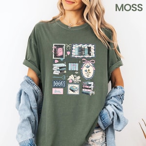 May include: Moss green t-shirt featuring a collage of book-themed illustrations. The design includes stacks of books, a pink bow, and the words "BOOKS love" in a pink rectangle. The shirt has rolled-up sleeves.