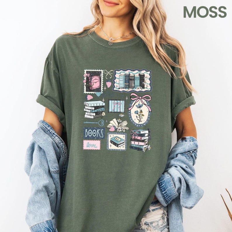 May include: Moss green t-shirt featuring a collage of book-themed illustrations. The design includes stacks of books, a pink bow, and the words "BOOKS love" in a pink rectangle. The shirt has rolled-up sleeves.
