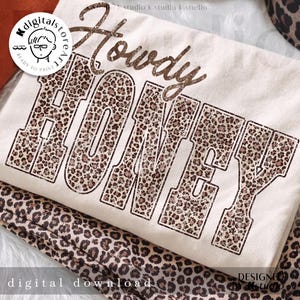 以下が含まれることがあります： クリーム色のTシャツ。茶色のかすれたフォントで「Howdy Honey」と書かれています。「Honey」の文字はヒョウ柄で埋められています。「digital download」の文字が下部にあります。