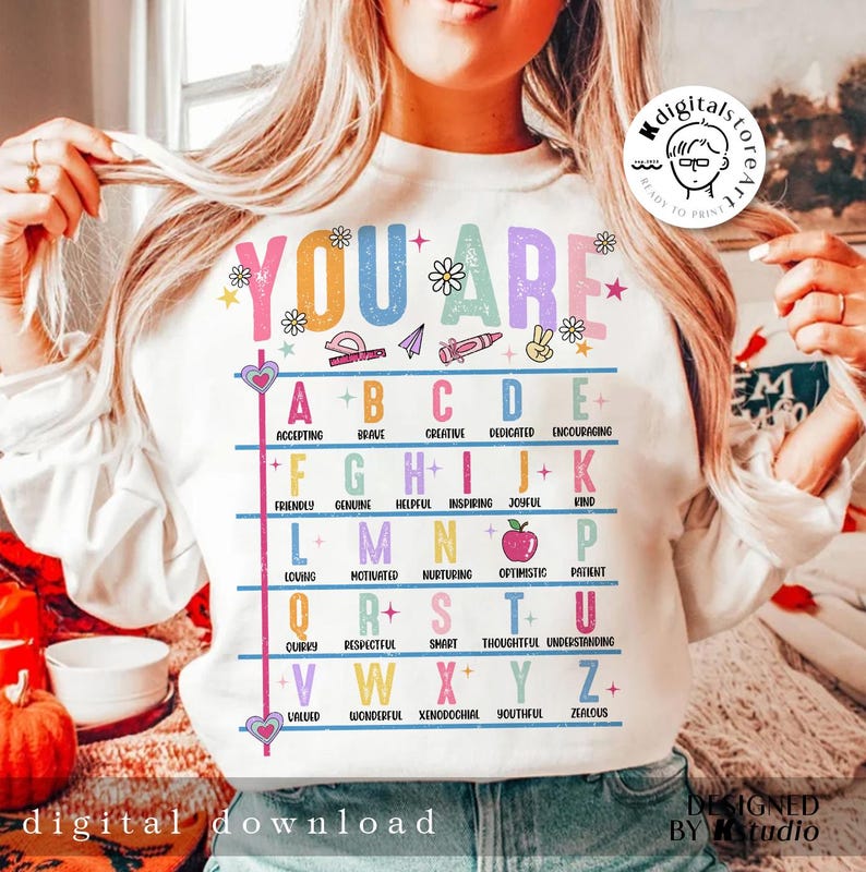 May include: White sweatshirt with the text "YOU ARE" in rainbow colors and a colorful alphabet chart with positive adjectives for each letter. The chart includes illustrations of a protractor, a paper airplane, a crayon, a peace sign, and an apple.
