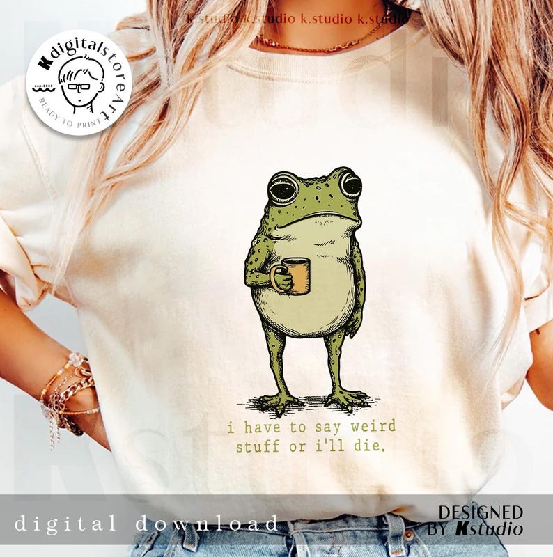 May include: Cream-colored sweatshirt featuring a green frog holding a yellow mug. The frog has a grumpy expression and is covered in spots. The text "i have to say weird stuff or i'll die" is printed below the frog. Digital download.