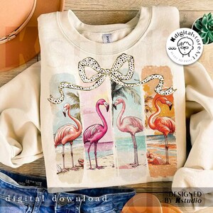 May include: Cream-colored sweatshirt featuring a colorful flamingo design. The graphic includes four flamingos on a beach, with a bow and the words "DIGITAL DOWNLOAD" at the bottom. The design is in a vintage style.