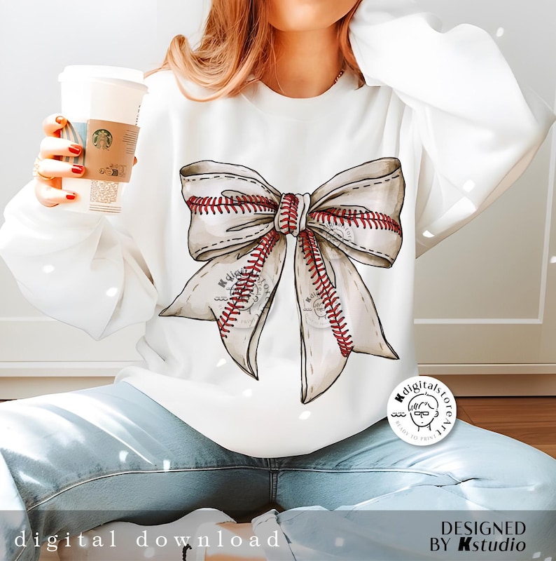 May include: White sweatshirt with a large beige bow with red stitching, resembling a baseball. The bow is centered on the sweatshirt.