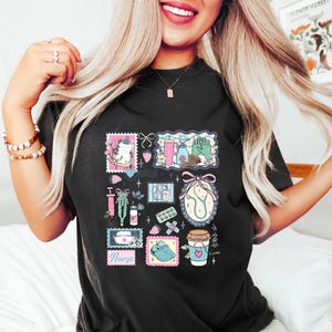 Op de afbeelding: Zwart T-shirt met een medisch thema collage ontwerp. Het ontwerp bevat postzegels met een stethoscoop, een spuit, pillen en een koffiekopje. Het woord "Nurse" is ook zichtbaar in het ontwerp.