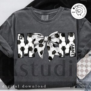 Peut inclure: Un t-shirt gris avec un motif de ballon de football noir et blanc qui &eacute;pelle "MOM" avec un n&oelig;ud noir au milieu. Le num&eacute;ro "12" est sur le "M" et le nom "JAME" est sur le "M".