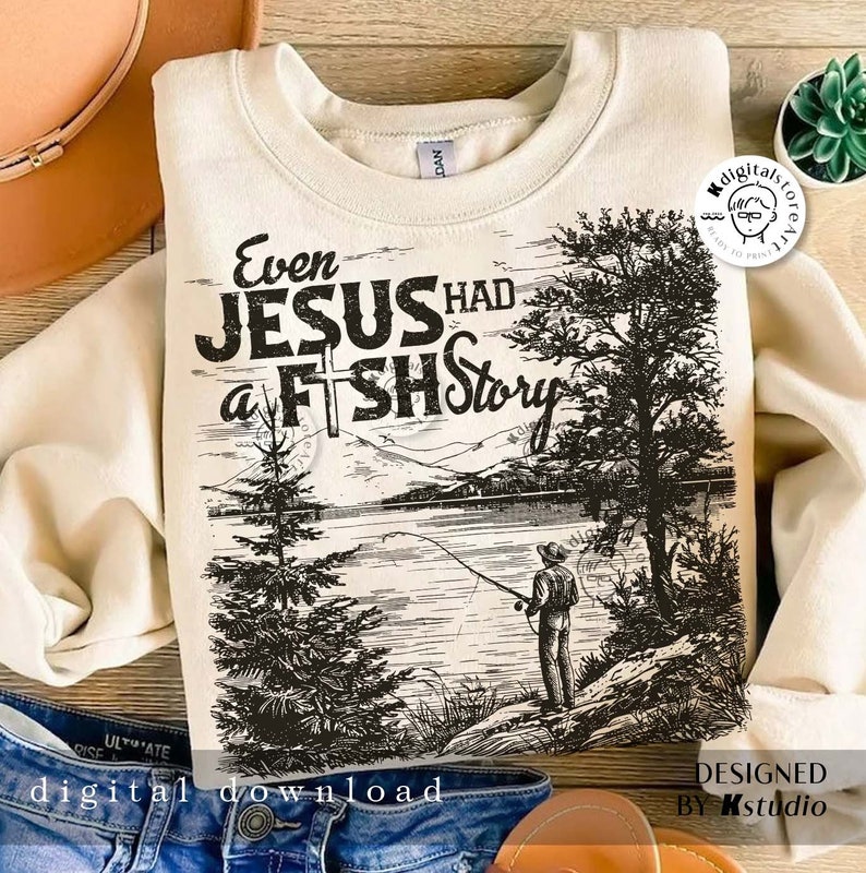 May include: A cream-colored sweatshirt with a black and white graphic design of a lake scene with a fisherman. The text "Even Jesus Had a Fish Story" is printed on the sweatshirt.