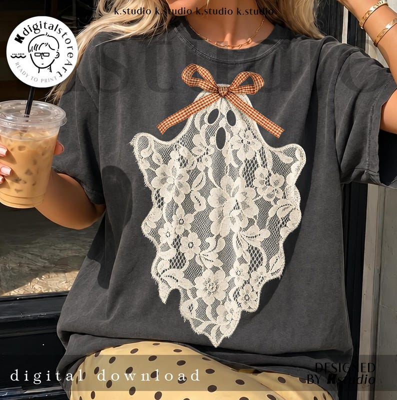 May include: A charcoal gray t-shirt featuring a large, white, lace-patterned ghost graphic centered on the chest. The ghost is adorned with a small, brown and white checkered ribbon bow at the top. The fabric has a faded, vintage-style appearance.
