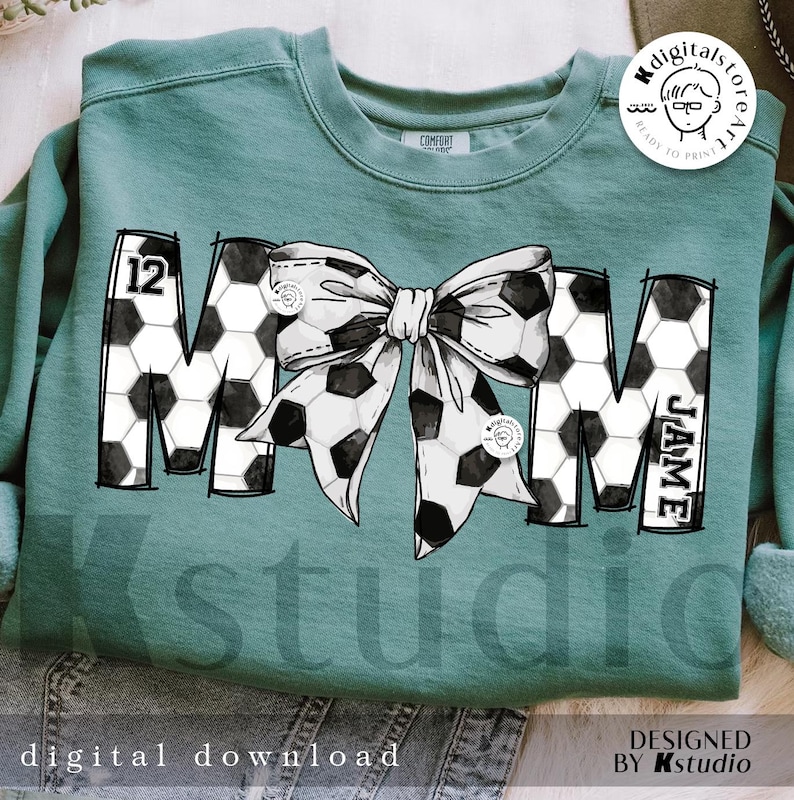Peut inclure: Un sweat-shirt turquoise avec un motif noir et blanc du mot "MOM" avec un motif de ballon de football et un n&oelig;ud. Le num&eacute;ro "12" est sur le "M" et le nom "JAIME" est sur le "M".