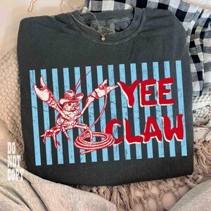 May include: Dark gray sweatshirt with a graphic of a cowboy crawfish with the words "Yee Claw" in red. The crawfish is wearing a cowboy hat and holding a lasso. Blue vertical stripes are behind the crawfish and text.