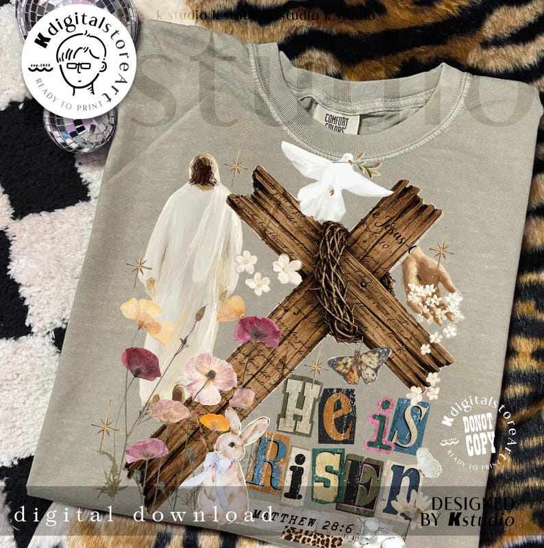 May include: A light green t-shirt featuring a graphic design with a wooden cross, flowers, a dove, and a bunny. The words "He is Risen" are displayed in colorful letters. The text "digital download" and "Matthew 28:6" are also visible.