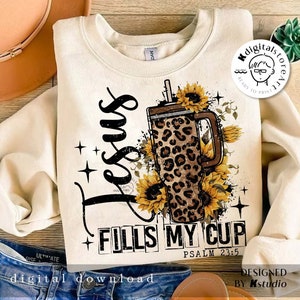 Może przedstawiać: Kremowa bluza z nadrukiem graficznym. Projekt zawiera słowa "Jesus Fills My Cup" i Psalm 23:5, kubek w panterkę, słoneczniki i gwiazdy. Widoczne są r&oacute;wnież słowa "digital download".
