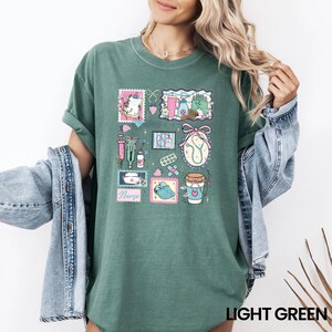 Op de afbeelding: Lichtgroen T-shirt met een collage-ontwerp met een medisch thema. Het ontwerp bevat illustraties van medische benodigdheden en het woord "Nurse". Het T-shirt heeft een relaxte pasvorm.