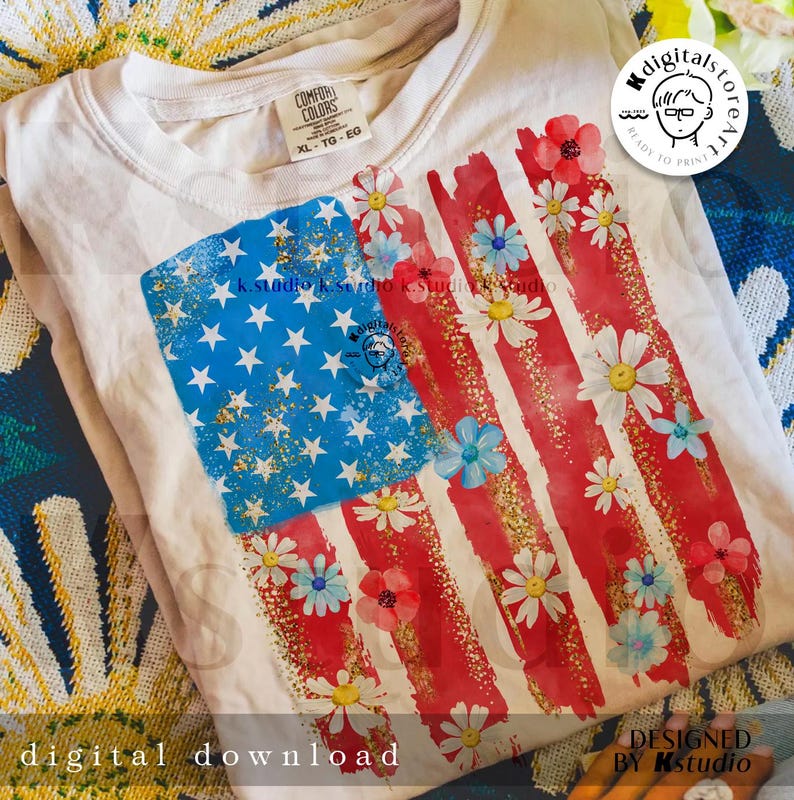 Puede incluir: Una camiseta blanca con un dise&ntilde;o de bandera americana roja, blanca y azul. La bandera est&aacute; pintada con un aspecto desgastado y tiene margaritas blancas y flores azules esparcidas a su alrededor. La etiqueta dice "COMFOR COLORS XL-TG-EG".
