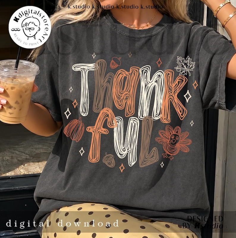 K&ouml;nnte beinhalten: Ein anthrazitfarbenes Kurzarm-T-Shirt mit dem Schriftzug Thankful in wei&szlig;em und orangefarbenem Linien-Design. Das Motiv enth&auml;lt Illustrationen eines Truthahns, von Eicheln, einem Ahornblatt und kleinen Rauten, die um den Text verteilt sind.