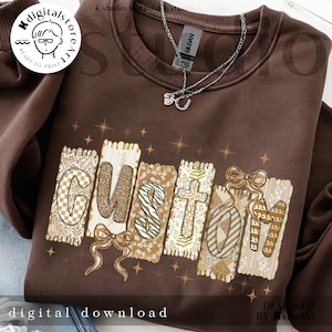 Può includere: Una felpa marrone con la scritta "CUSTOM" in un carattere decorativo. Le lettere sono in vari motivi e colori, tra cui glitter dorati, stampa zebrata e disegni floreali. È visibile una collana d'argento.